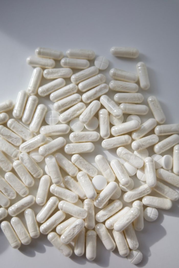 A pile of white capsules and tablets scattered on a light surface, ideal for medical themes.